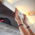 Close up of hands putting luggage in an overhead bin