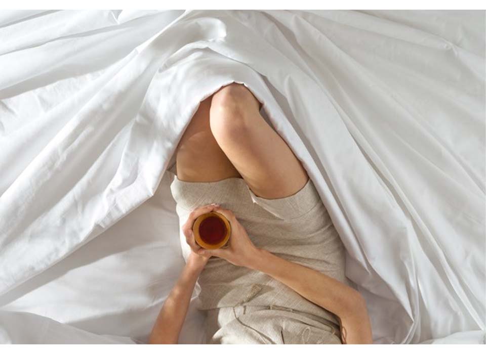 Aerial view of woman drinking coffee in a bed outfitted in Saatva sheets