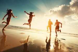 Four people running on the beach toward the ocean