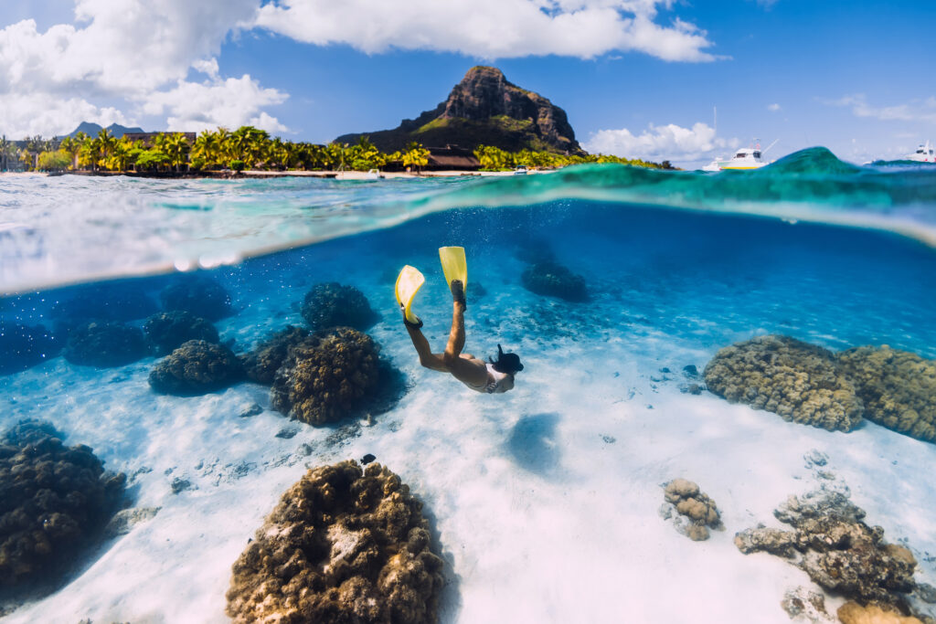 Image half above and half below the water, showing a woman scuba diving in the waters of Mauritus