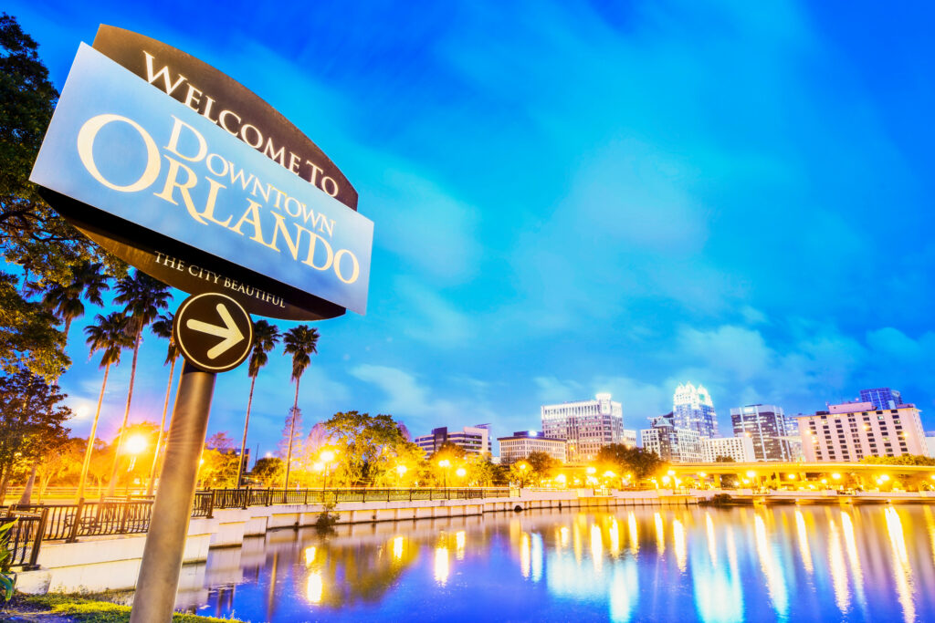 Low-angle view of sign saying "Welcome to Downtown Orlando" with the Orlando skyline in the background