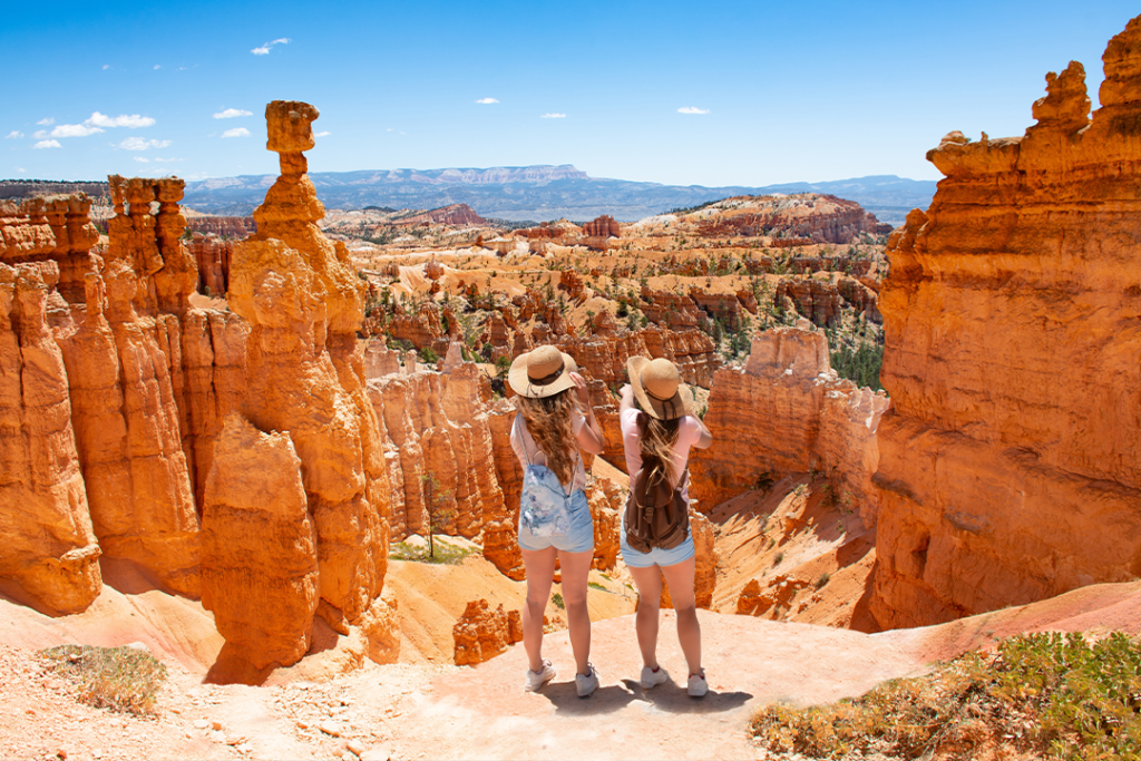 Girls on vacation hiking trip. Friends standing next to Thor's Hammer hoodoo on top of mountain looking at beautiful view. Bryce Canyon National Park, Utah, USA