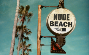 aged and worn vintage photo of nude beach sign with palm trees