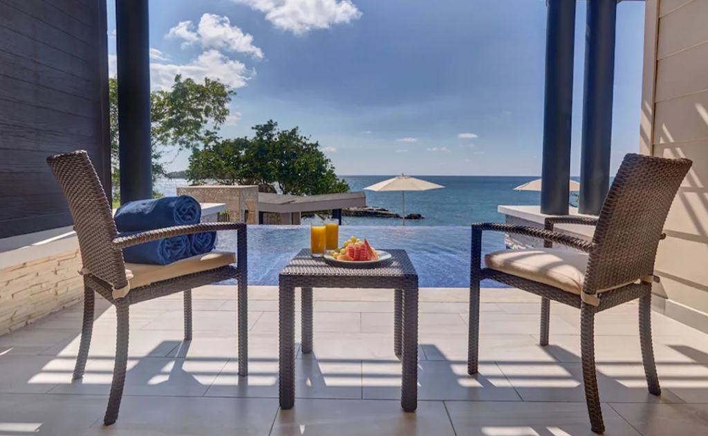 Two chairs and a table set up next to a private pool with drinks and food on the table overlooking the ocean