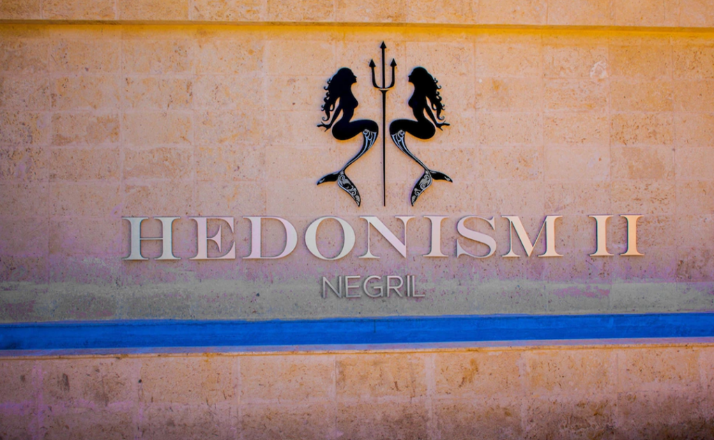 Hedonism II Resort name on brick with mermaids and a trident.