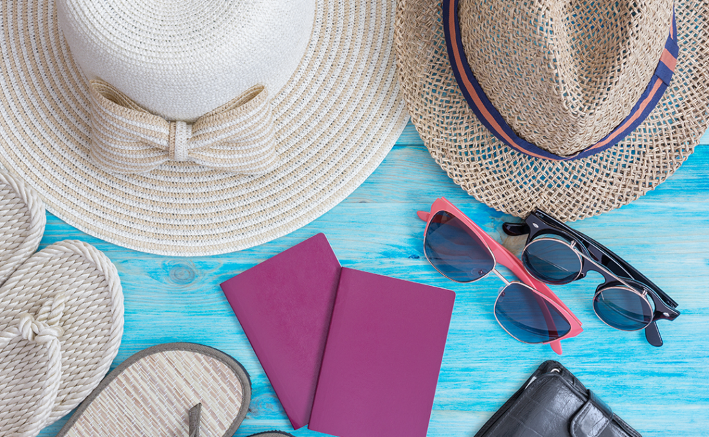 Summer hats and other travel accessories on blue wooden background