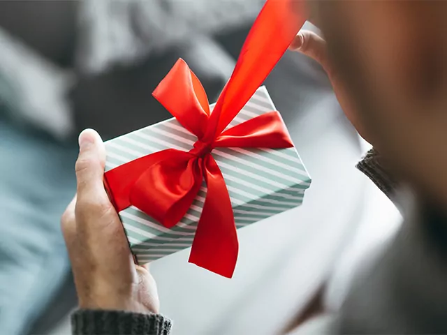 Over the shoulder view of a man opening a small giftbox with a red ribbon