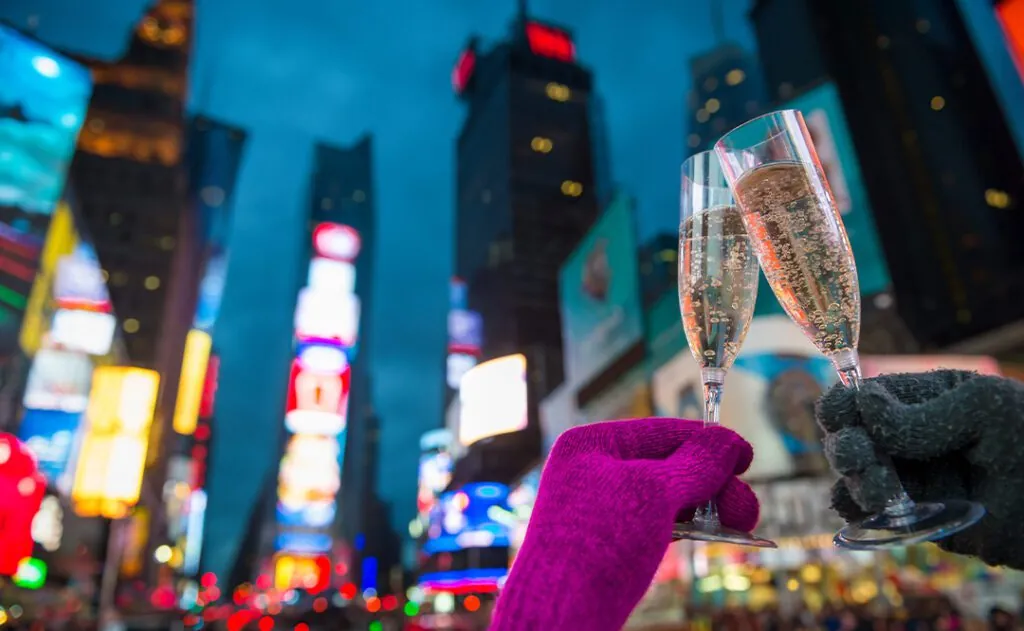 Gloved hands holding up Champagne glasses in a Mew Year’s Eve toast against the bright lights of Times Square, New York City