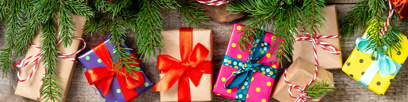 Christmas background with gift boxes Packed in different colors on a brown wooden table. Christmas or new year gifts under the fir branches. The view from the top.